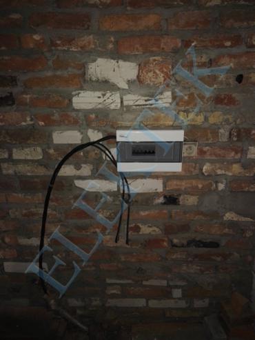 Nowa, biała skrzynka rozdzielcza zamontowana na starej, ceglanej ścianie z widocznymi przewodami.