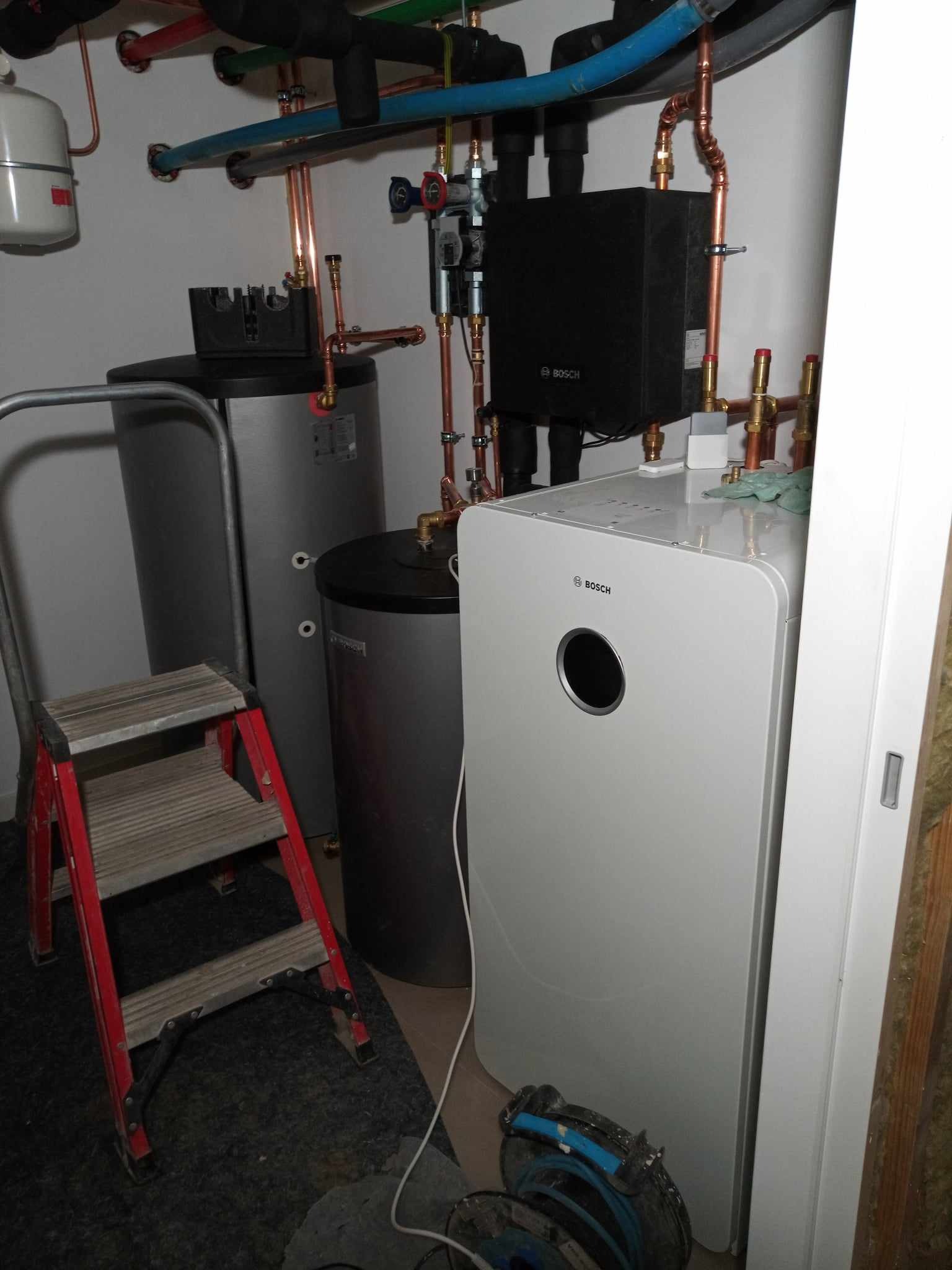 Zainstalowana, nowoczesna pompa ciepła Bosch w kotłowni, z widocznymi rurami miedzianymi, zbiornikami buforowymi i drabiną malarską.