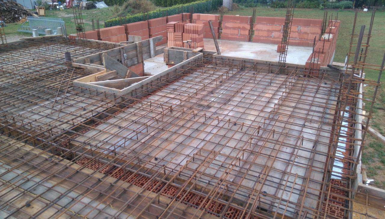 Zbrojenie fundamentów domu jednorodzinnego z drewnianym szalunkiem i częściowo wymurowanymi ścianami z czerwonej cegły. Widok z góry na plac budowy.