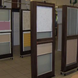 Ekspozycja różnorodnych osłon okiennych: rolety wewnętrzne w różnych kolorach i wzorach, żaluzje poziome oraz plisy, prezentowane na stojakach w salonie.