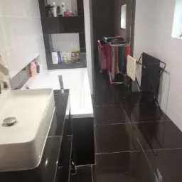 Nowoczesna łazienka z białą armaturą, czarnymi płytkami podłogowymi i suszarką na pranie w tle.