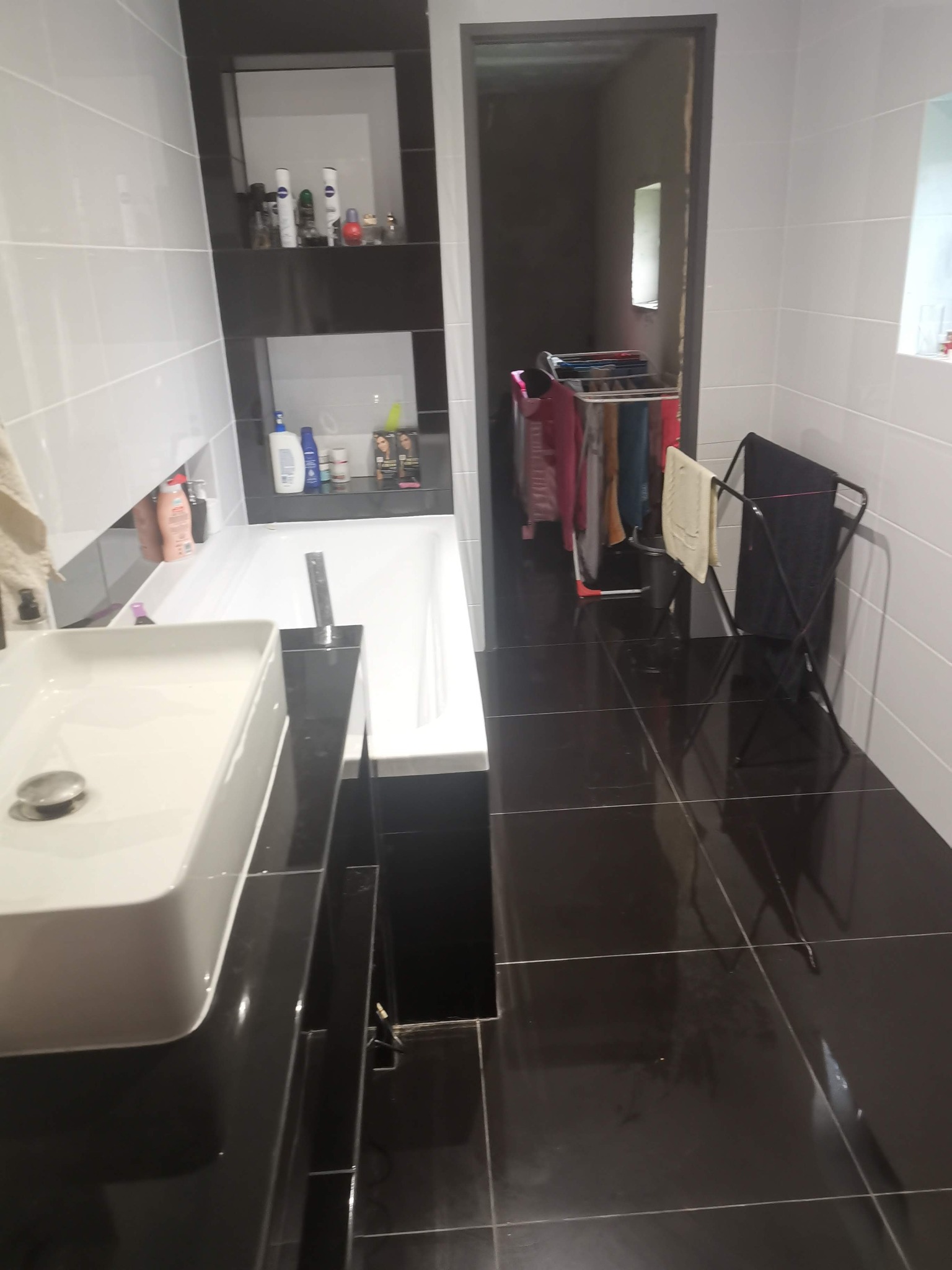 Nowoczesna łazienka z białą armaturą, czarnymi płytkami podłogowymi i suszarką na pranie w tle.