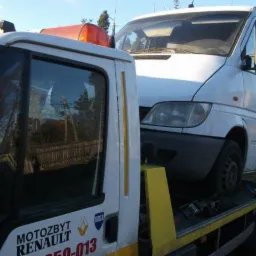 Biała laweta z pomarańczowym kogutem przewozi białego busa. Widoczne logo firmy na lawecie.