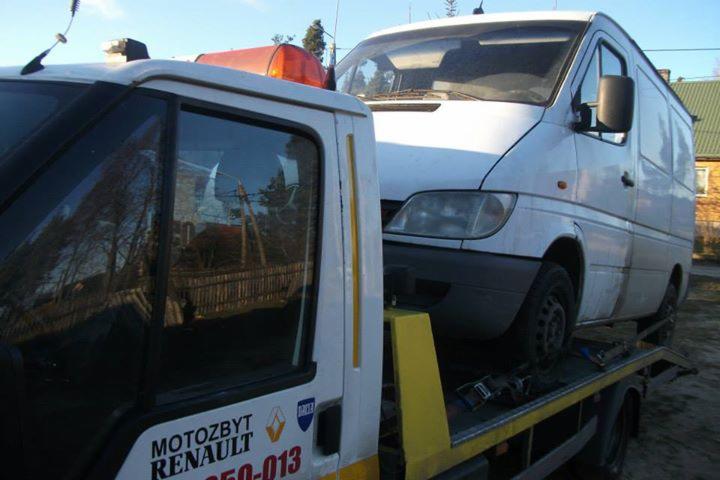 Biała laweta z pomarańczowym kogutem przewozi białego busa. Widoczne logo firmy na lawecie.