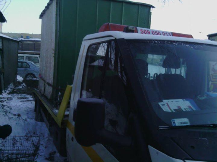 Laweta z kontenerem na platformie, widoczny numer telefonu na dachu pojazdu, zimowa sceneria.