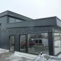 Nowoczesny budynek w kolorze antracytowym z dużymi przeszkleniami i bramą rolowaną, widok z zewnątrz w zimowej scenerii.