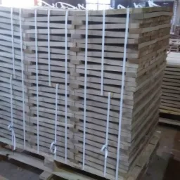 Stosy świeżo przetartego drewna ułożone na paletach, zabezpieczone białymi taśmami w hali produkcyjnej.