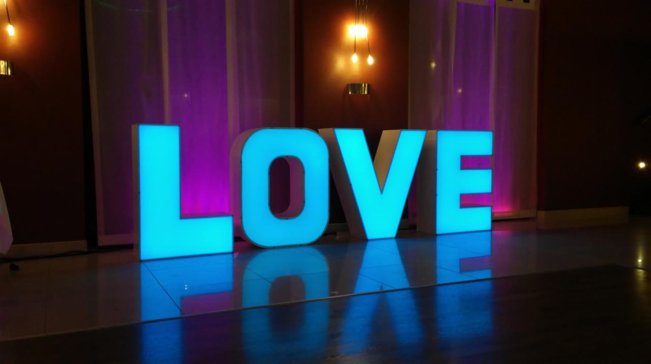 Dekoracja sali weselnej: podświetlane na turkusowo litery LOVE, odbijające się w błyszczącej podłodze, fioletowe tło.