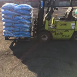 Wózek widłowy Clark transportuje paletę z workami w niebieskiej folii. Widoczny napis 'RE-TRANS Skład Opału'.