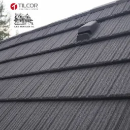 Szary dach pokryty metalową dachówką z widocznym kominkiem wentylacyjnym, logo producenta w lewym górnym rogu.