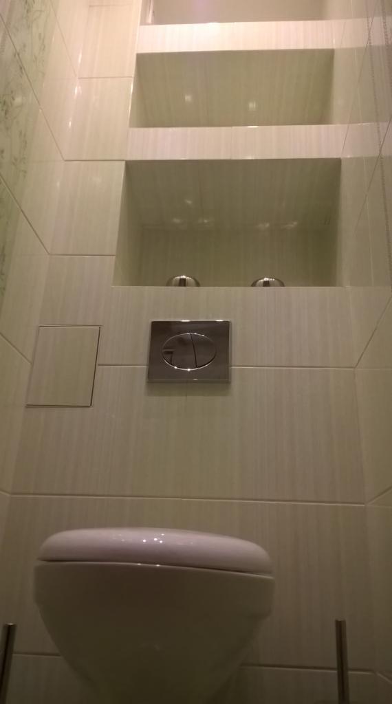 Wnętrze łazienki po remoncie: biała toaleta, płytki imitujące drewno, wnęki w ścianie. Nowoczesny design i funkcjonalność.