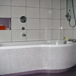 Biała wanna obłożona mozaiką w łazience z białymi płytkami, widoczna armatura, półka w ścianie z kosmetykami, kabina prysznicowa z transparentną szybą.