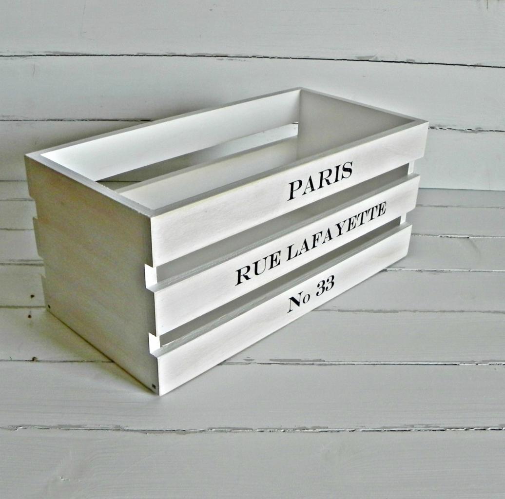 Biała drewniana skrzynka dekoracyjna z napisem 'Paris Rue Lafayette No 33' na tle białych desek.