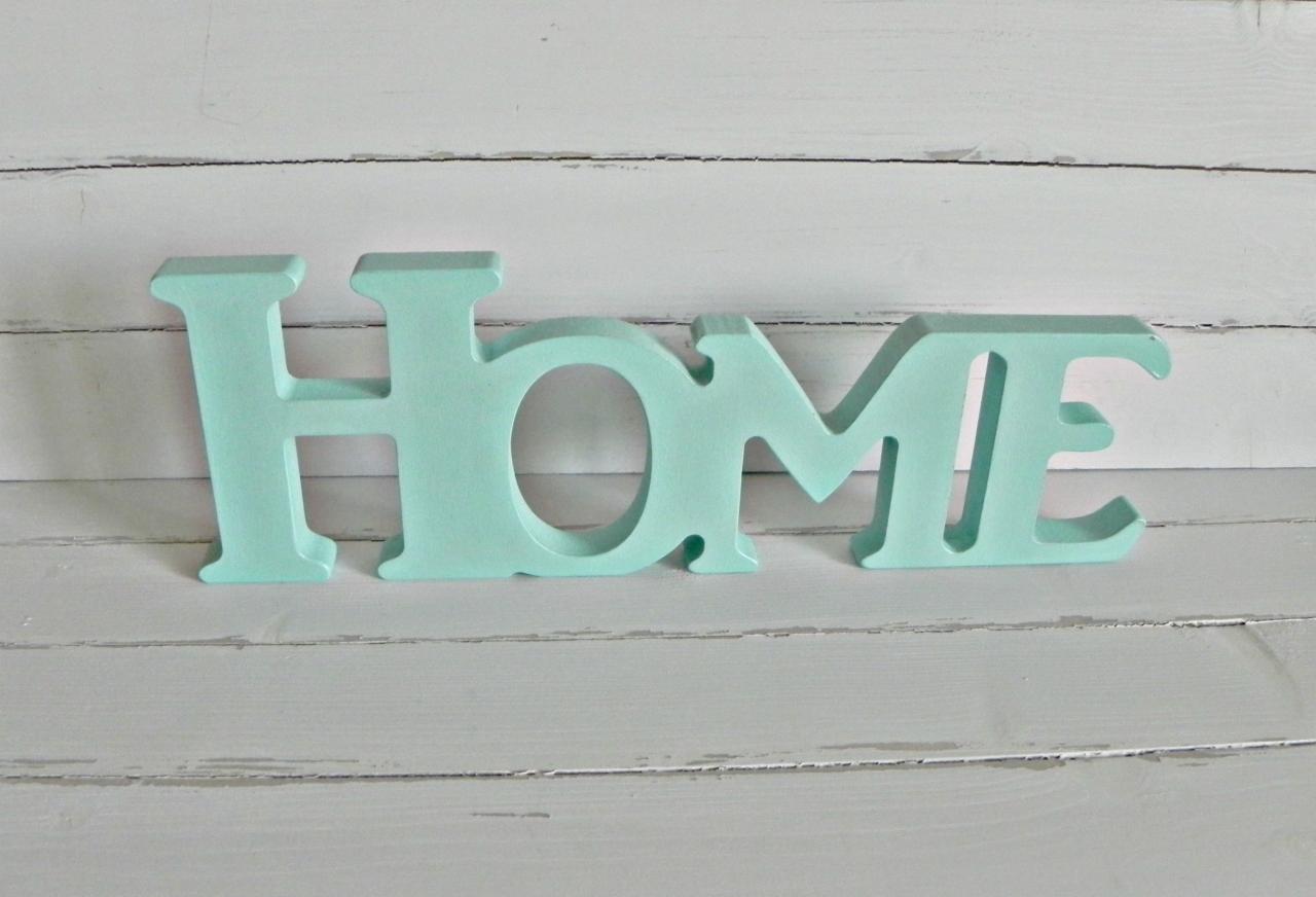 Turkusowy, drewniany napis 'HOME' na tle szarych desek. Dekoracja wnętrza w stylu skandynawskim, minimalistyczny design, pastelowe kolory, bliski kadr.
