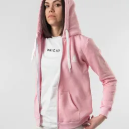 Kobieta w różowej rozpinanej bluzie z kapturem i białym t-shircie z nadrukiem 'UNICAT' pozuje na jasnym tle.