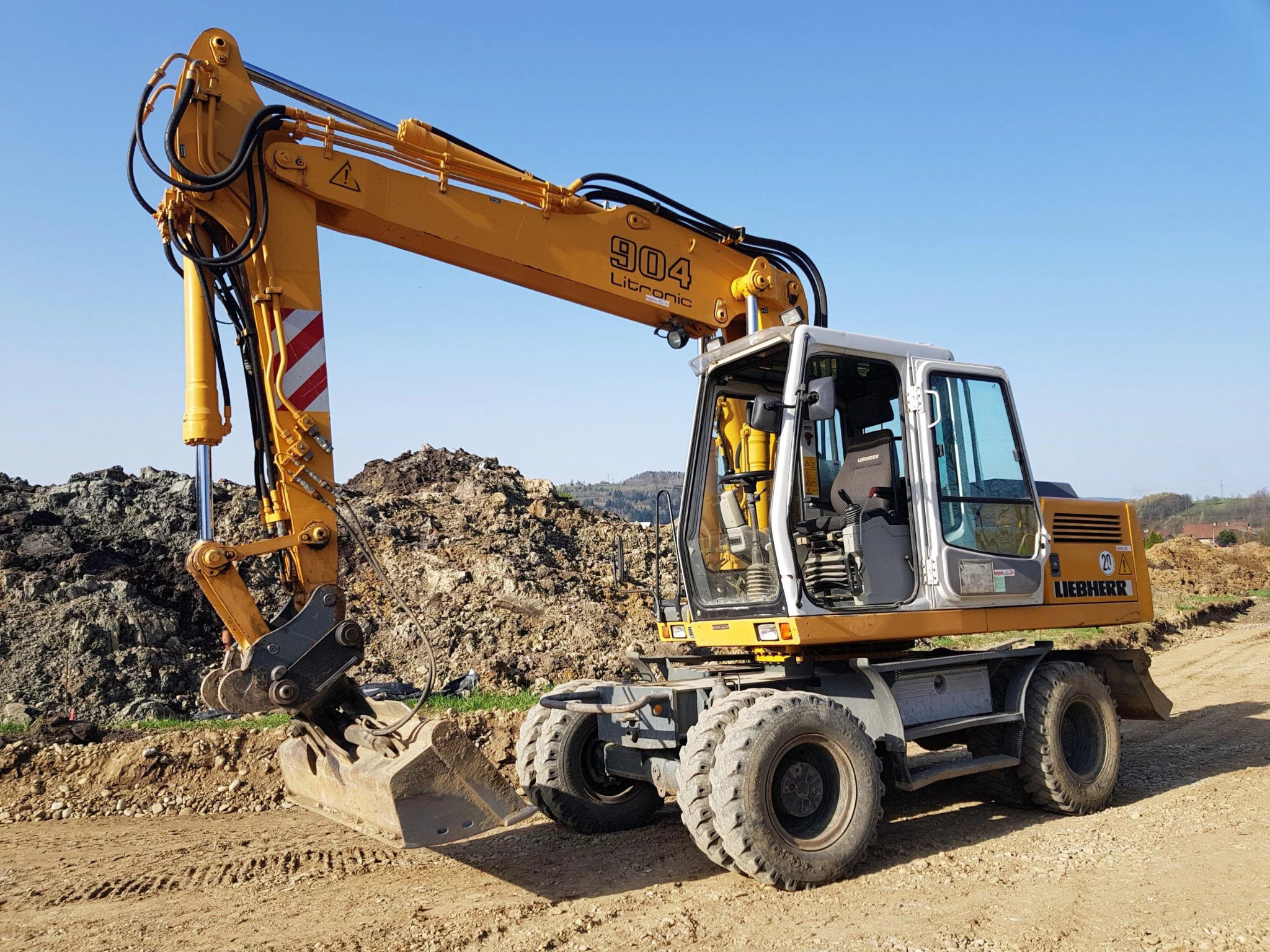 Żółta koparka kołowa Liebherr 904 Litronic na placu budowy, z widocznym stosem ziemi w tle i śladami opon na piaszczystym podłożu.