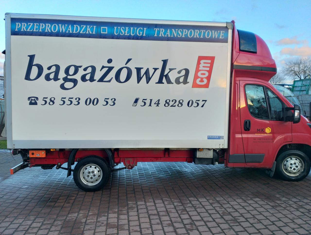 Czerwony samochód dostawczy z białą zabudową i napisem 'bagażówka.com' oraz numerami telefonów, zaparkowany na brukowanej nawierzchni. Widoczne logo firmy MK Przeprowadzki na drzwiach kabiny.