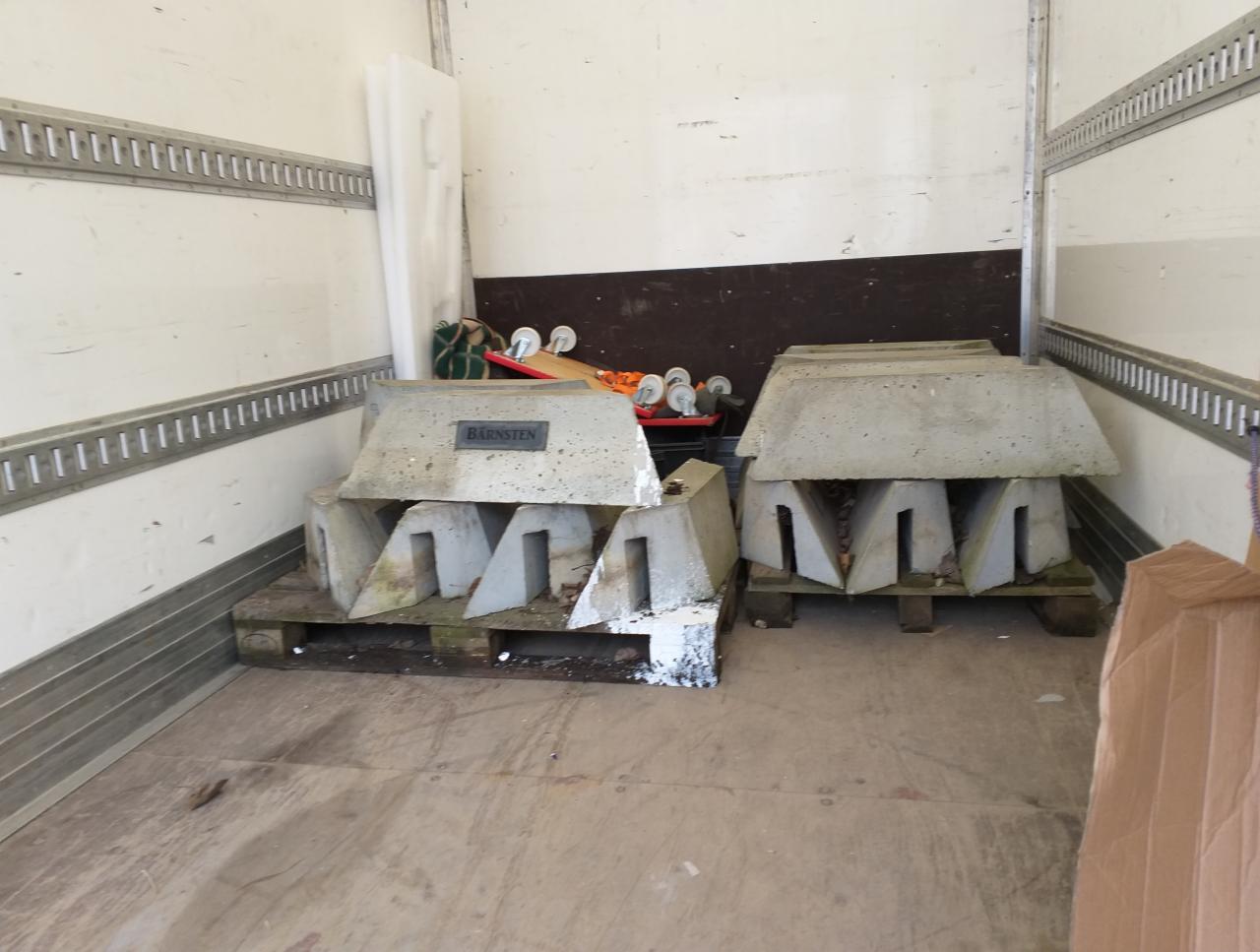 Wnętrze paki transportowej z zabezpieczeniami betonowymi na paletach, widoczne ślady użytkowania i zabrudzenia.