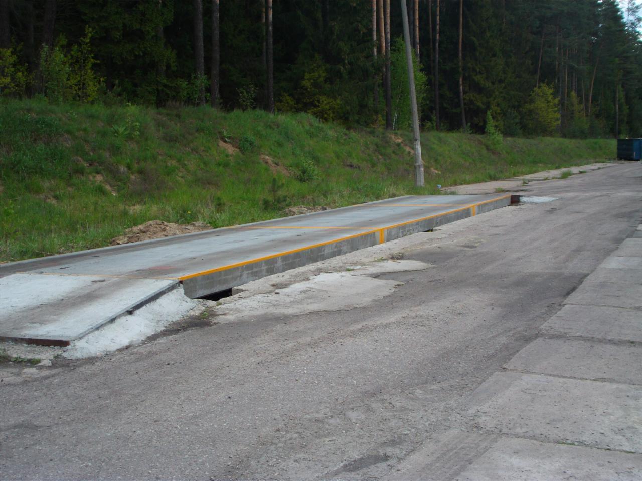 Ważka samochodowa z żółtymi krawędziami na tle zieleni i drzew. Betonowa konstrukcja wkomponowana w asfaltową drogę.