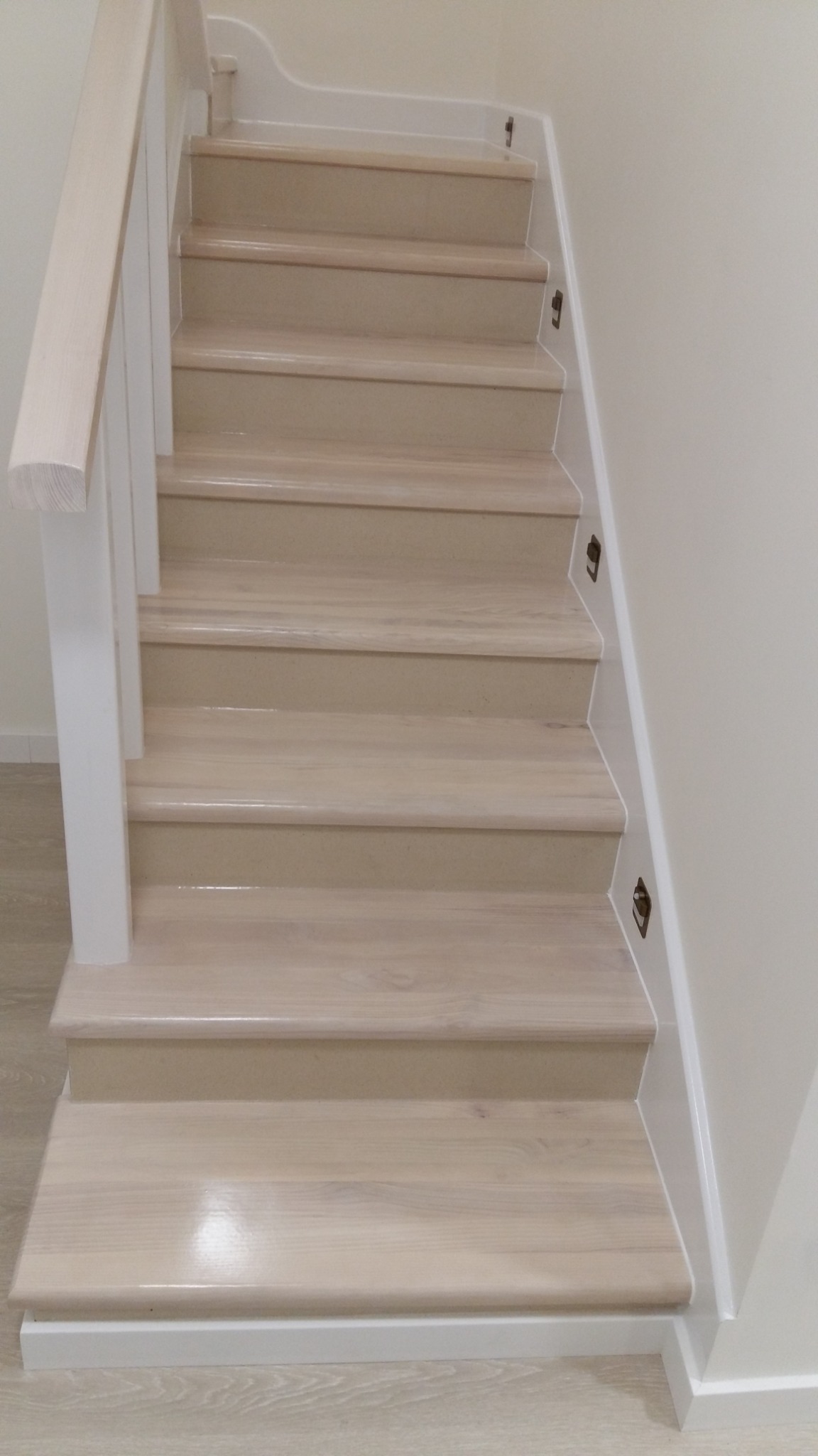 Jasne, drewniane schody z białymi balustradami i listwami przypodłogowymi, widok z dołu, ukazujący detale wykończenia i subtelne oświetlenie.