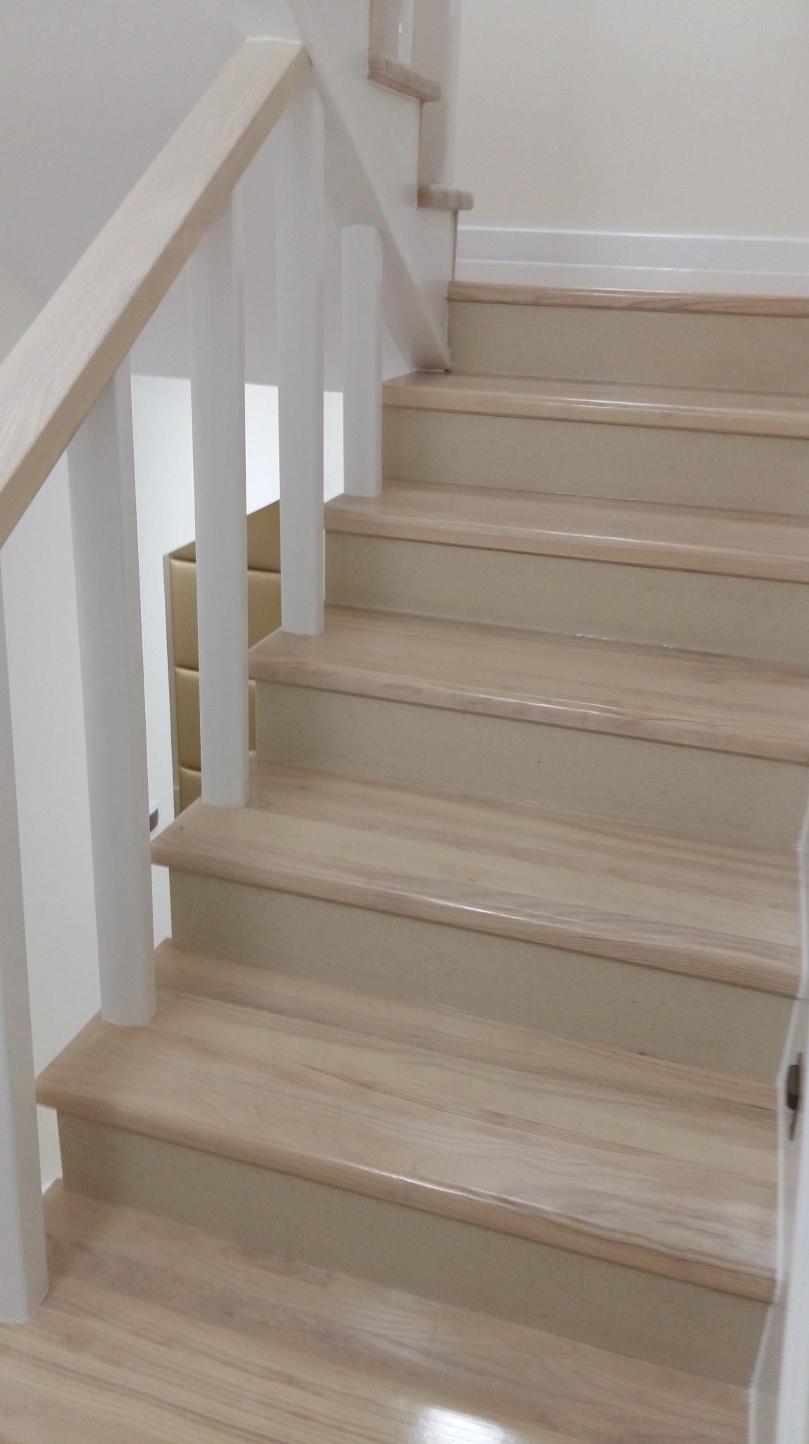 Jasne, drewniane schody z białymi balustradami, widok z dołu. Naturalne oświetlenie podkreśla strukturę drewna. Minimalistyczny design.