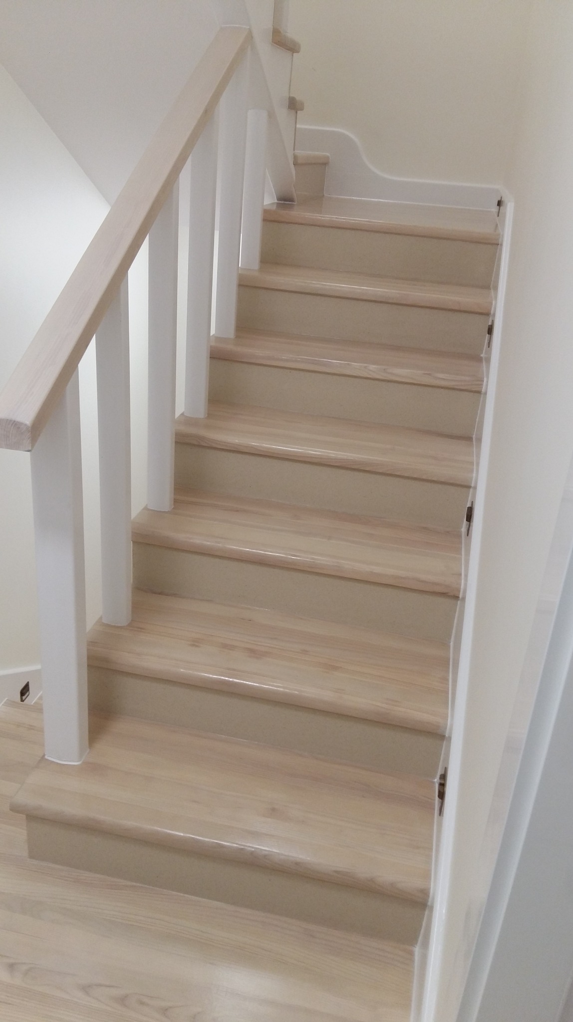 Jasne, drewniane schody z białą balustradą, widok z dołu. Stopnie o gładkiej powierzchni, delikatne oświetlenie, minimalistyczny design. Detal wykończenia wnętrza.