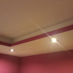 Dawwoj - Częściowy widok pokoju z pomalowanymi na różowo ścianami i sufitem z wbudowanymi lampami. Czerwone pasy dekoracyjne na suficie.