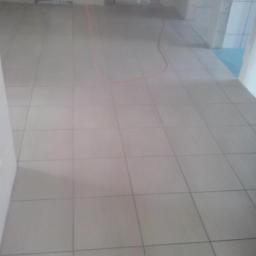 Dawwoj - Ułożona jasna podłoga z płytek w trakcie remontu. Widoczne wiadro z farbą i przewód na podłodze. Minimalistyczny styl wykończenia wnętrz.