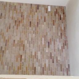Dawwoj - Ściana wyłożona mozaiką z podłużnych, beżowo-brązowych elementów, tworzących dekoracyjny wzór. Widoczny fragment ściany i sufitu pomalowane na biało.