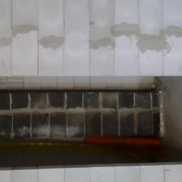 Dawwoj - Wnętrze w trakcie budowy: białe bloczki ścienne, widoczna instalacja rur w otworze, surowy beton na podłodze. Etap prac instalacyjnych przed dalszym wykończeniem.