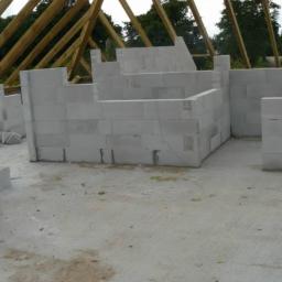 Dawwoj - Wnętrze domu w trakcie budowy. Ściany z białych bloczków, drewniany szkielet dachu. Widoczne surowe wykończenie podłogi i ściany w trakcie wznoszenia.