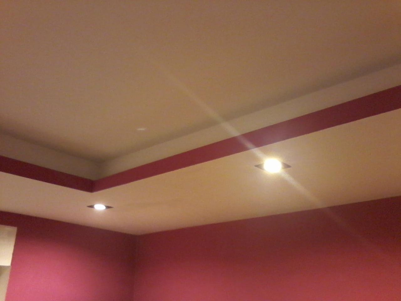 Częściowy widok pokoju z pomalowanymi na różowo ścianami i sufitem z wbudowanymi lampami. Czerwone pasy dekoracyjne na suficie.