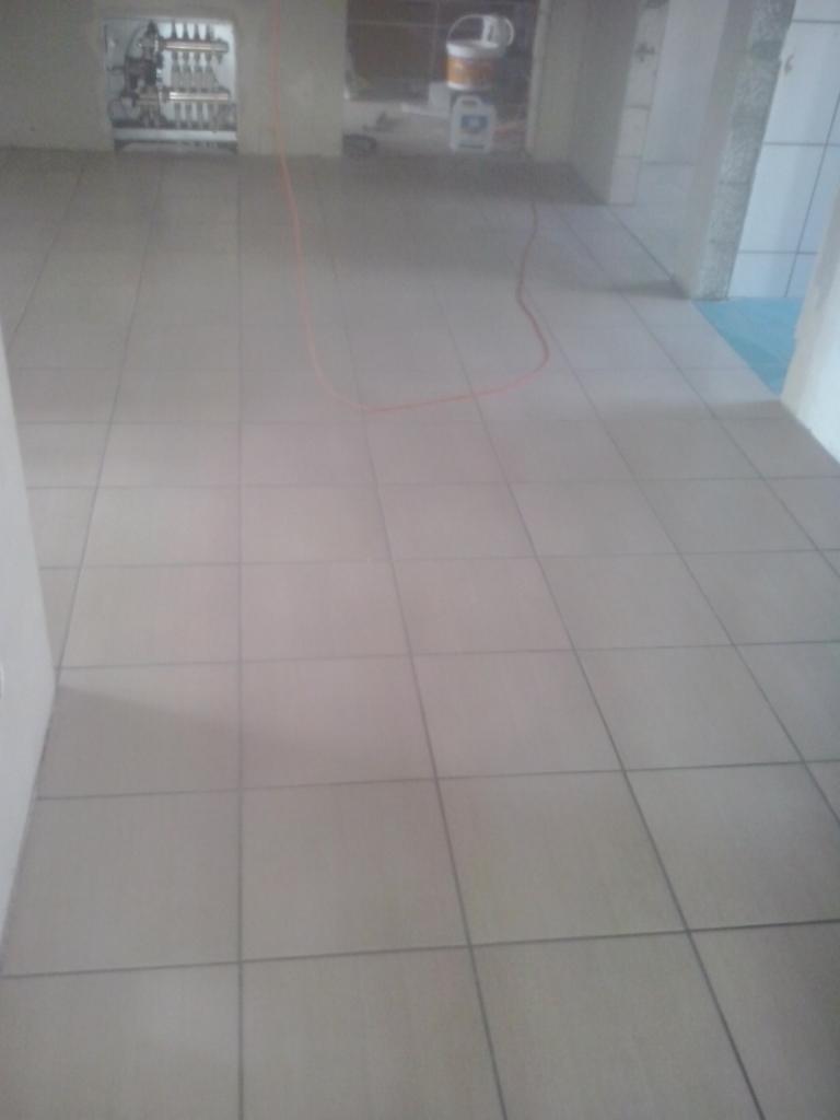 Ułożona jasna podłoga z płytek w trakcie remontu. Widoczne wiadro z farbą i przewód na podłodze. Minimalistyczny styl wykończenia wnętrz.