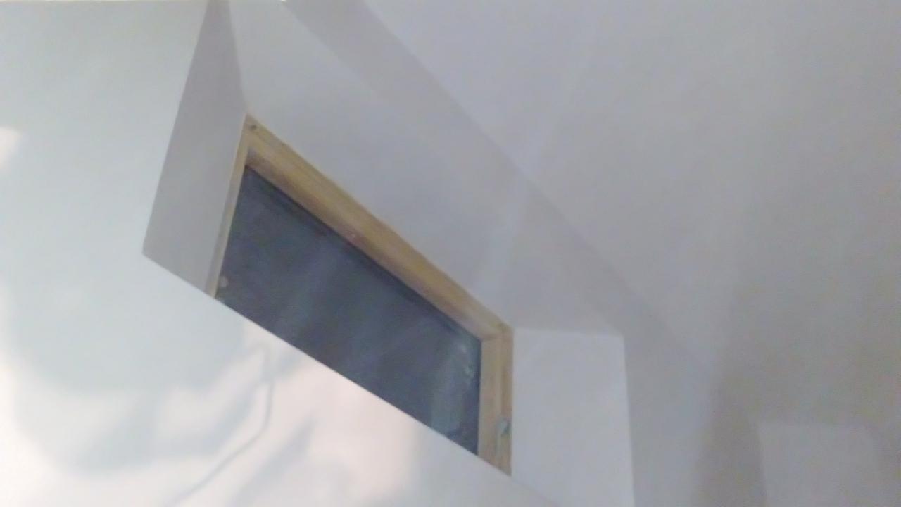 Nietypowe okno w ścianie po remoncie, z drewnianą ramą i głębokim osadzeniem, widziane pod kątem. Białe ściany i sufit, neutralne oświetlenie.