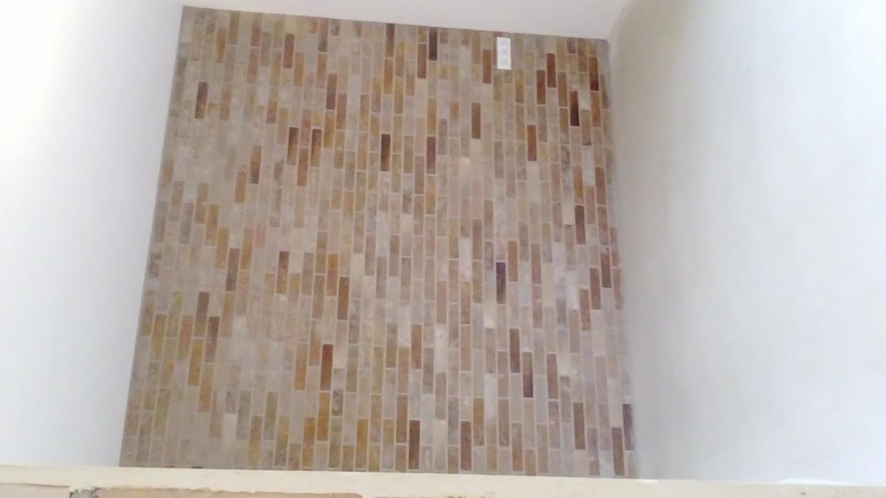 Ściana wyłożona mozaiką z podłużnych, beżowo-brązowych elementów, tworzących dekoracyjny wzór. Widoczny fragment ściany i sufitu pomalowane na biało.