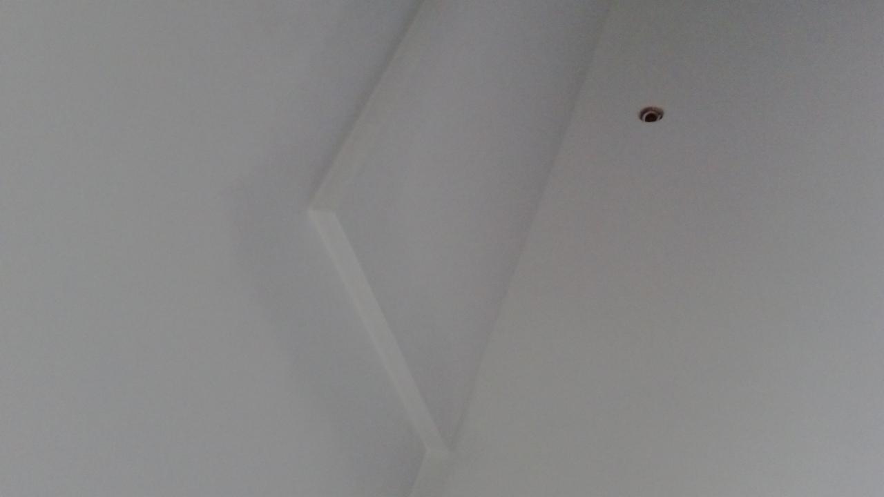 Gładka, biała powierzchnia sufitu z subtelnym załamaniem i punktowym oświetleniem. Minimalistyczne wykończenie wnętrza.