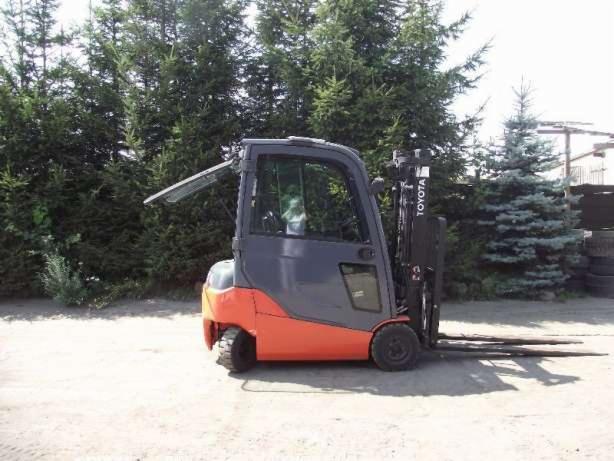 Nowy wózek widłowy Toyota z otwartą kabiną, pomarańczowo-szary, na żwirowym podłożu, w tle iglaki i opony.