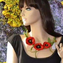 Manekin w czarnej sukience prezentuje naszyjnik z filcowanymi makami na tle abstrakcyjnej ściany w odcieniach żółci i fioletu. Nietypowe tło dodaje zdjęciu unikalności.