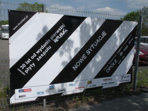 Czarno-biały baner koncertowy z ukośnymi pasami, informujący o 30-leciu płyty zespołu Republika, na ogrodzeniu z siatki, z widocznymi logotypami sponsorów.