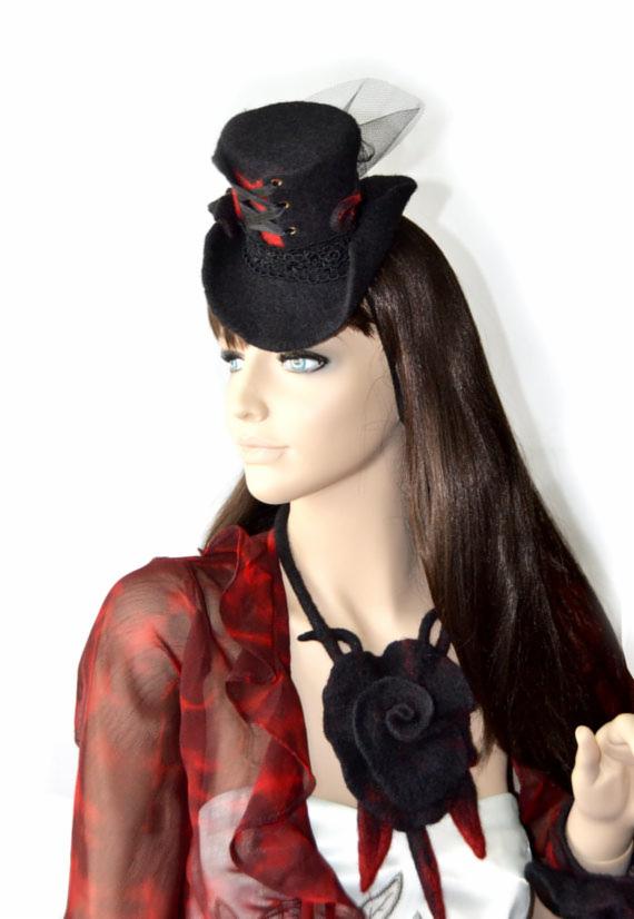 Manekin z czarnym mini cylindrem z czerwonymi akcentami i naszyjnikiem z filcowanej róży, ubrany w czerwoną bluzkę. Detal stroju w stylu gotyckim.