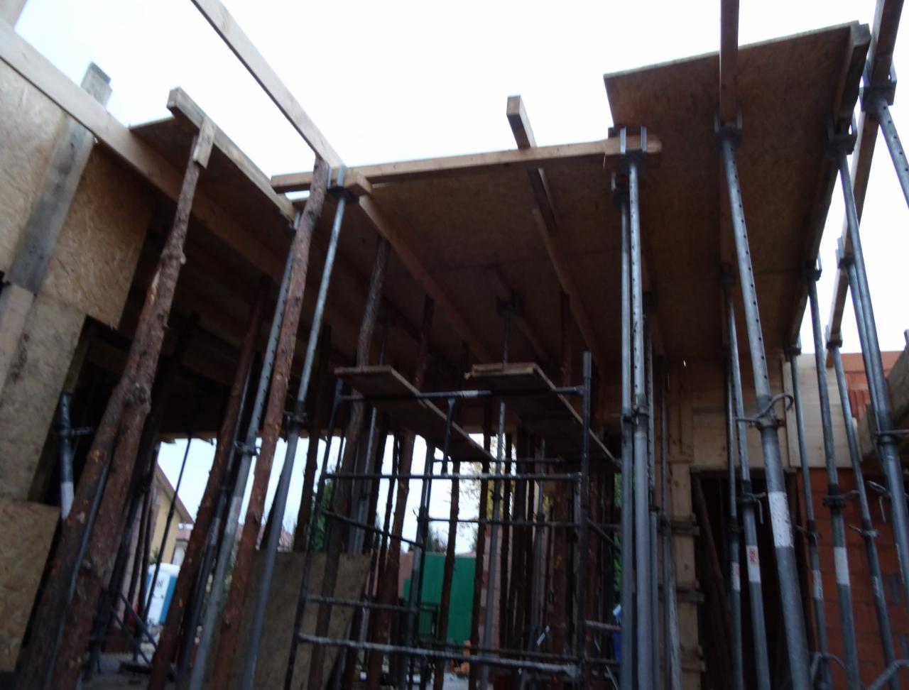 Szczegółowe ujęcie szalunku stropowego z podporami stalowymi i drewnianymi, widoczne elementy konstrukcyjne i rusztowanie, etap budowy w surowym stanie.