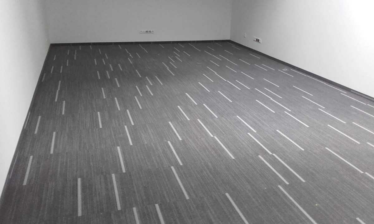 Szara wykładzina dywanowa w pasy w pustym, jasnym pomieszczeniu biurowym, widok na całą podłogę.