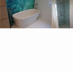 Nowoczesna łazienka z wolnostojącą wanną na tle turkusowej ściany z motywem bąbelków i kabiną prysznicową wykończoną mozaiką w odcieniach niebieskiego.