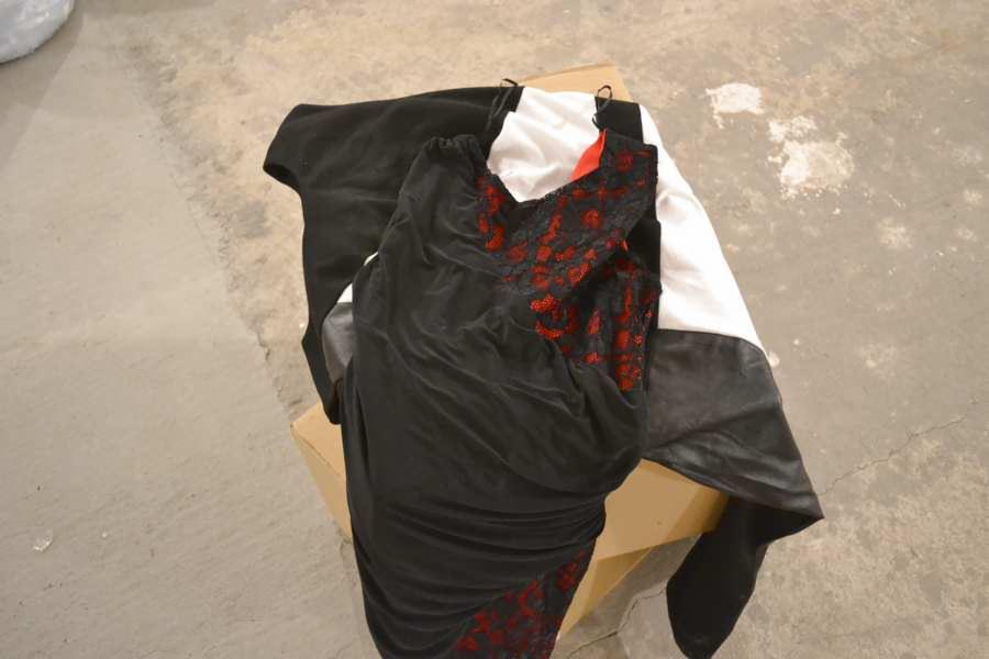 Ułożone ubrania na kartonowym pudełku: czarna sukienka z koronką, biała koszula i czarna bluza. Widoczne detale materiałów i faktur. Minimalistyczne ujęcie na szarym tle.