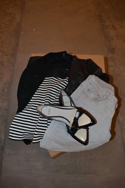 Stos ubrań na kartonie: dżinsy, bluzka w paski, czarna kurtka i lakierowane baleriny z beżowymi wstawkami. Ubrania używane, w dobrym stanie, gotowe do sprzedaży.