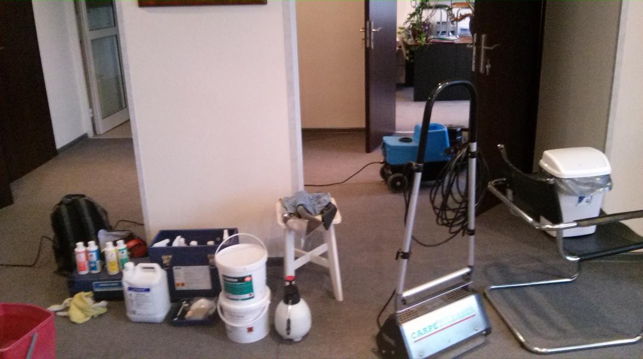 Sprzęt do czyszczenia dywanów i wykładzin: odkurzacz piorący, chemia, wiadro i krzesło. Przygotowanie do pracy w biurze. Widok na korytarz biurowy.