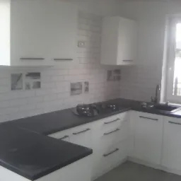 Nowoczesna kuchnia z białymi szafkami, czarnym blatem i białymi płytkami imitującymi cegłę, z elementami dekoracyjnymi na ścianie.