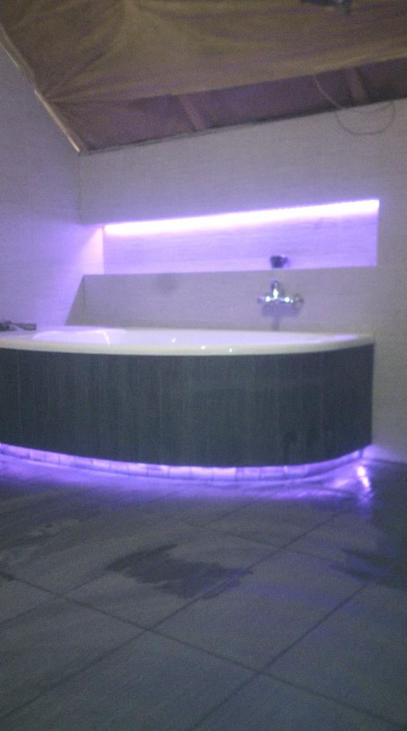 Nowoczesna łazienka z okrągłą wanną, podświetleniem LED i szarą podłogą. Bateria umywalkowa nad wanną. Sufit częściowo zakryty folią.