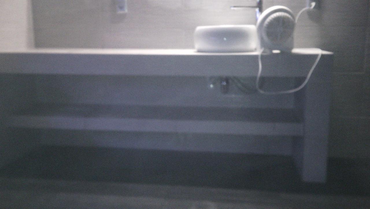 Minimalistyczna łazienka: biała umywalka nablatowa i wentylator na długim blacie z półkami w szaro-białej tonacji.