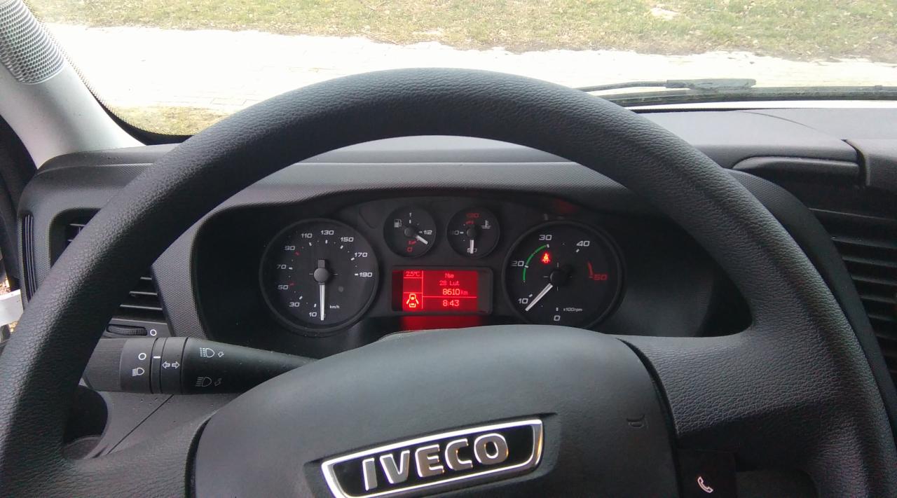 Wnętrze kabiny Iveco: deska rozdzielcza z prędkościomierzem, obrotomierzem i wyświetlaczem, kierownica z logo. Widok z perspektywy kierowcy na zegary i elementy sterujące pojazdu.